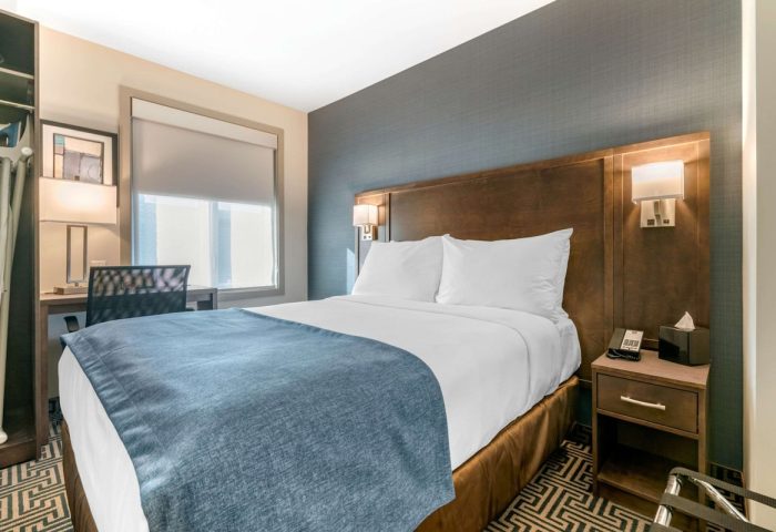 Quality Inn Centre-Ville gay-friendly hotel room. Queen bed with blue cover, desk, and nightstand. Comfortable stay for gay travelers.