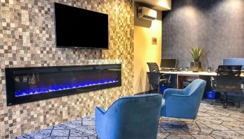 Quality Inn Centre-Ville's gay-friendly hotel lobby. Blue chairs face a modern fireplace and TV. Business center in the background.