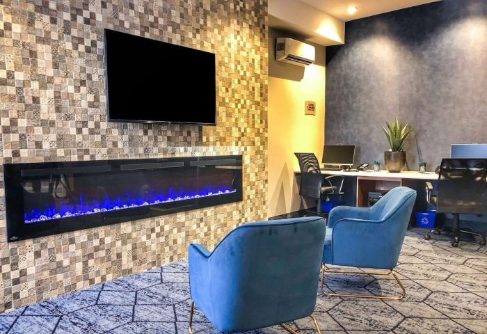Quality Inn Centre-Ville's gay-friendly hotel lobby. Blue chairs face a modern fireplace and TV. Business center in the background.