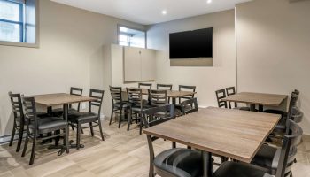 Quality Inn Centre-Ville gay-friendly hotel dining area. Tables with black chairs, a TV, and storage in a neutral-toned room.