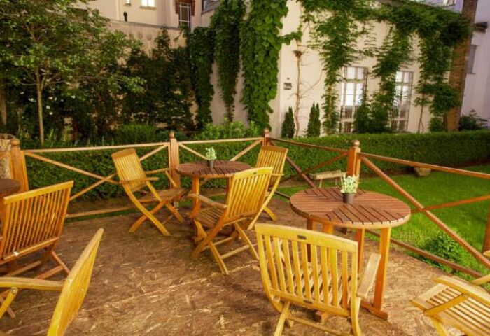 Outdoor seating at Quentin Design Hotel Berlin, a gay-friendly space. Tables and chairs on a patio, surrounded by greenery. Relaxing atmosphere.