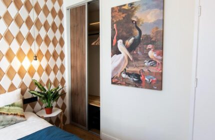 Quentin Golden Bear Hotel room. Diamond pattern wall, art of birds, sliding closet doors, bed, and side table. Gay-friendly hotel interior.