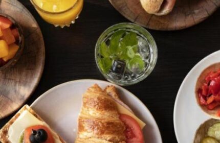 Quentin Golden Bear Hotel's gay-friendly breakfast. Croissant, sandwich, fruit, juice, and cracker on a dark table. Gay travel advice.