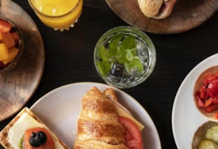 Quentin Golden Bear Hotel's gay-friendly breakfast. Croissant, sandwich, fruit, juice, and cracker on a dark table. Gay travel advice.