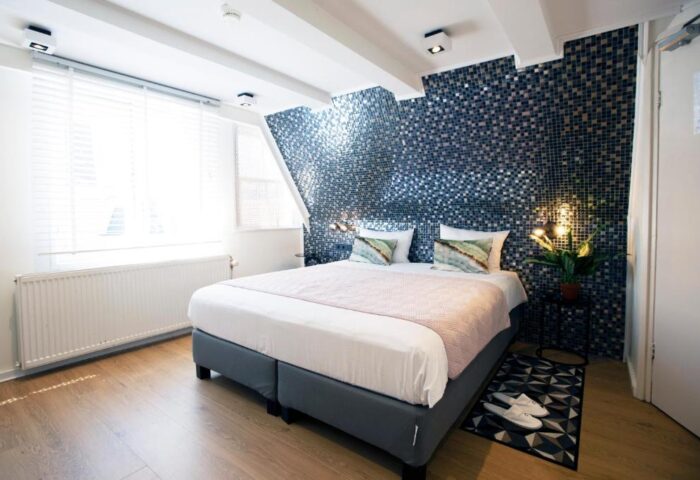 Quentin Golden Bear Hotel room. Gay-friendly hotel bedroom with mosaic wall, double bed, and natural light. Ideal for gay men's travel.