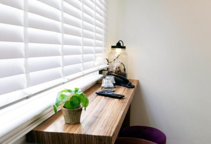 Quentin Golden Bear Hotel's gay-friendly room: desk with plant, lamp, phone, glasses, and remote by the window. Cozy hotel interior.