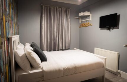 REM Hotel's gay-friendly room: Double bed with white linens, TV, colorful accent wall, and gray walls. A comfortable stay for gay travelers.