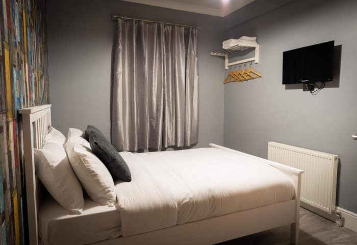 REM Hotel's gay-friendly room: Double bed with white linens, TV, colorful accent wall, and gray walls. A comfortable stay for gay travelers.