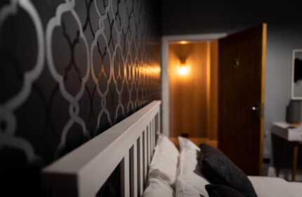 REM Hotel's bedroom detail. Gay-friendly hotel room with stylish wallpaper, white headboard, and open doorway. Ideal for gay travel lodging.