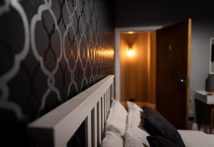 REM Hotel's bedroom detail. Gay-friendly hotel room with stylish wallpaper, white headboard, and open doorway. Ideal for gay travel lodging.