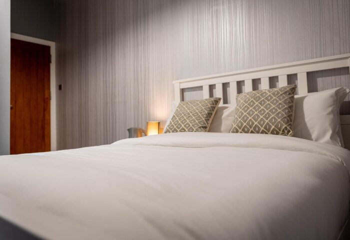 REM Hotel room with white bedding, pillows, headboard, and wallpaper. Gay-friendly hotel with a cozy interior.