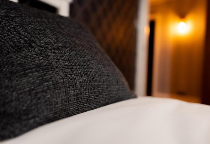 Close-up of a pillow on a bed at REM Hotel, a gay-friendly hotel. The room is illuminated by a warm light, creating a cozy atmosphere.