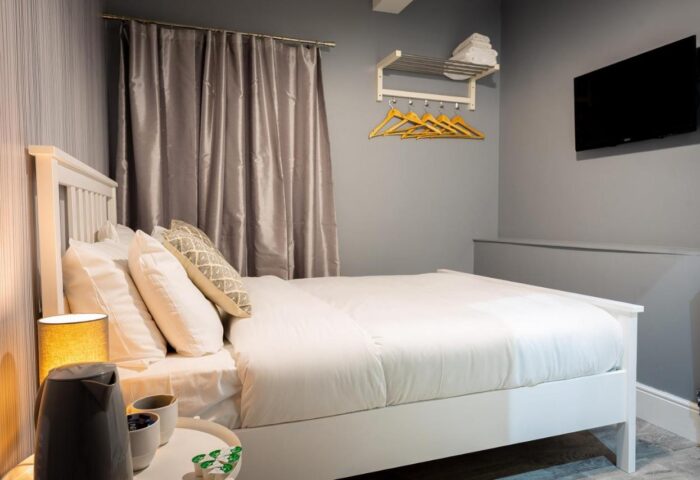 REM Hotel bedroom. Gay-friendly hotel room with a white bed, gray walls, TV, hangers, and bedside table with kettle. Cozy, modern design.