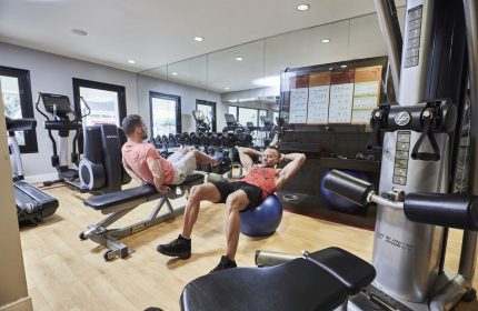 Gay-friendly RIU Plaza Fisherman's Wharf hotel gym. Two men exercising, one on a bench, the other on a ball. Fitness center with equipment.
