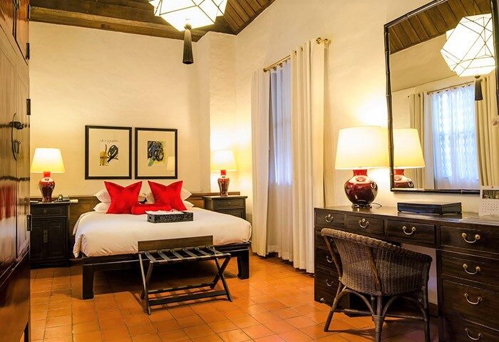 Rachamankha Hotel, a Relais & Châteaux member. Gay-friendly hotel room with king bed, red pillows, desk, and terracotta tile floor.