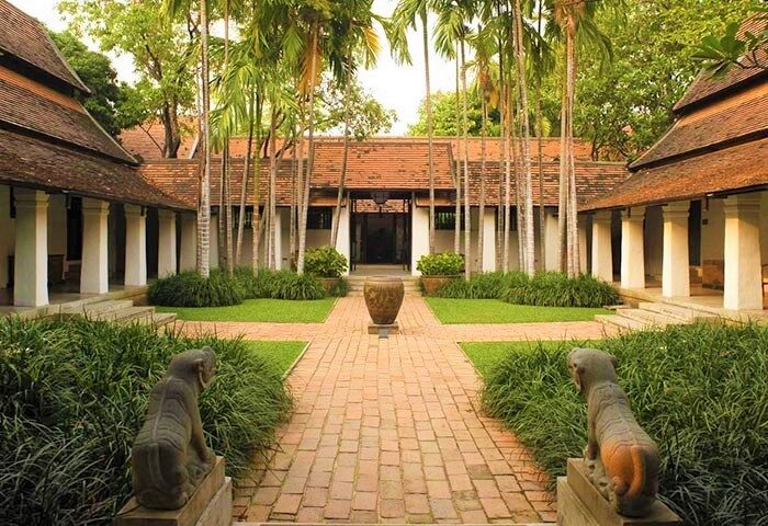 Rachamankha Hotel courtyard, a gay-friendly Relais & Châteaux member. Brick path, elephant statues, lush greenery, and traditional Thai architecture.
