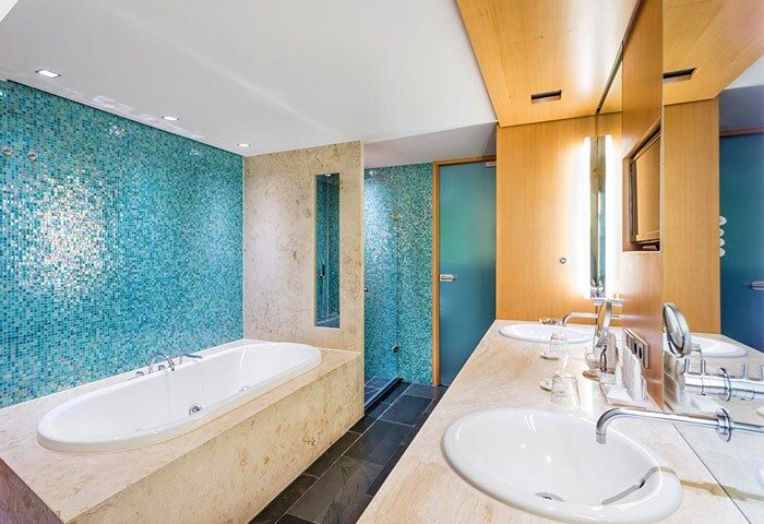 Bathroom at Radisson Collection Hotel, Berlin. Gay-friendly hotel with blue mosaic tile, bathtub, shower, and double sinks. Upscale design.