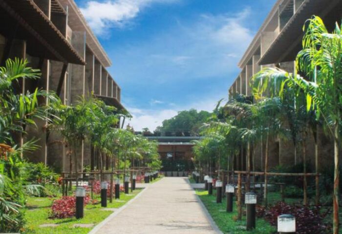 Pathway at the gay-friendly Railay Princess Resort & Spa. Tropical plants line the walkway between modern buildings under a blue sky.