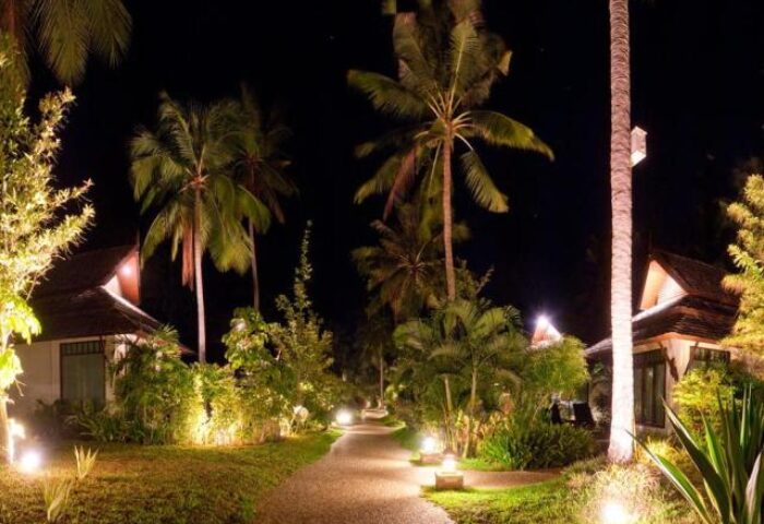 Night view of Railay Village Resort, a gay-friendly hotel. Path illuminated by lights, palm trees, and bungalows. Ideal for gay travel.