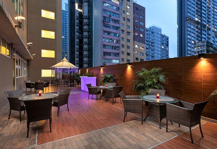 Ramada Hong Kong Harbour View gay-friendly hotel outdoor seating area. Tables and chairs on a patio with city views. Evening ambiance.