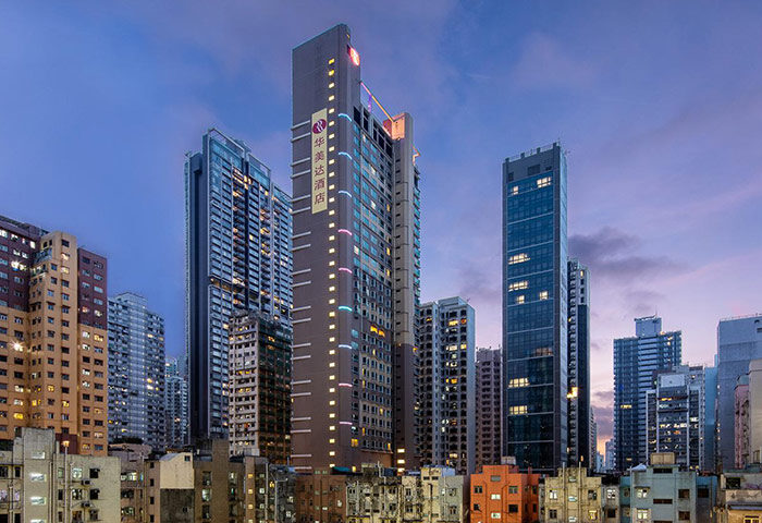 Hong Kong Harbour View Ramada Hotel exterior at dusk. Gay-friendly hotel with city skyline. Modern architecture, vibrant lights, travel destination.