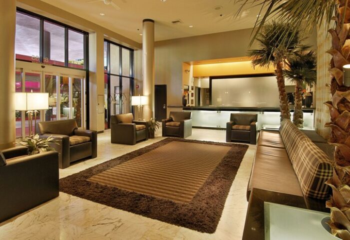 Ramada Plaza by Wyndham West Hollywood Hotel lobby. Brown leather chairs, rug, and couch. Gay-friendly hotel with suites. Palm trees.