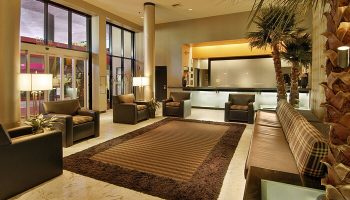 Ramada Plaza by Wyndham West Hollywood Hotel lobby. Brown leather chairs, rug, and couch. Gay-friendly hotel with suites. Palm trees.