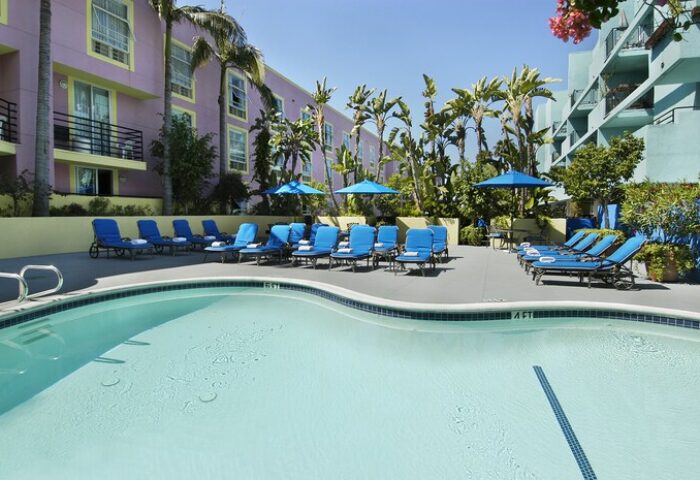 Ramada Plaza by Wyndham West Hollywood Hotel & Suites pool. Gay-friendly hotel with blue lounge chairs and palm trees for a relaxing vacation.