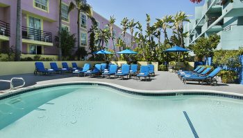 Ramada Plaza by Wyndham West Hollywood Hotel & Suites pool. Gay-friendly hotel with blue lounge chairs and palm trees for a relaxing vacation.