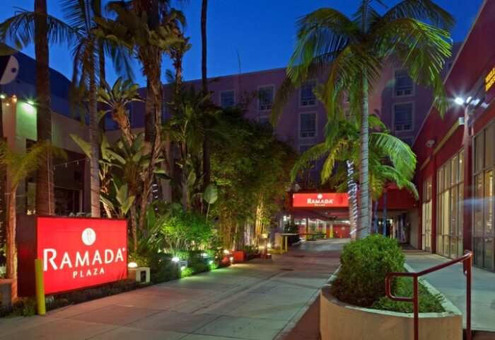 Ramada Plaza by Wyndham West Hollywood Hotel & Suites entrance. Gay-friendly hotel with palm trees and illuminated signage at night.