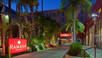 Ramada Plaza by Wyndham West Hollywood Hotel & Suites entrance. Gay-friendly hotel with palm trees and illuminated signage at night.