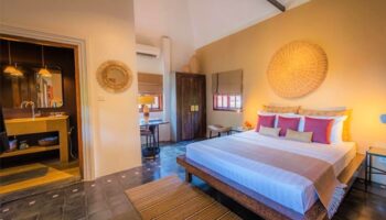Rambutan Resort Siem Reap gay-friendly hotel room. King bed, ensuite bathroom, desk, and woven decor in warm, inviting light.