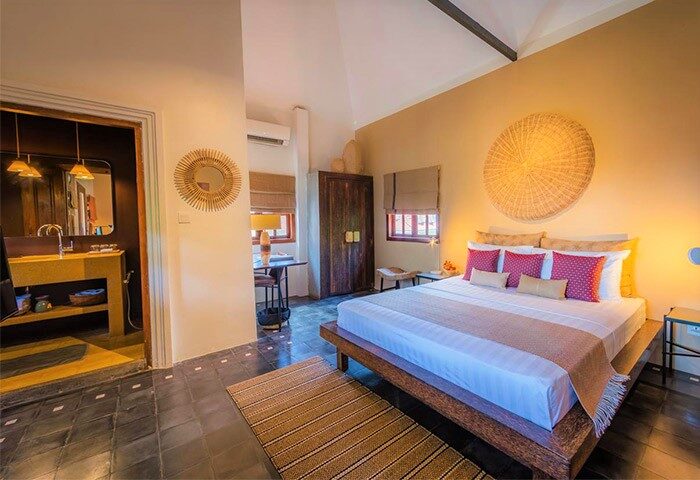 Rambutan Resort Siem Reap gay-friendly hotel room. King bed, ensuite bathroom, desk, and woven decor in warm, inviting light.