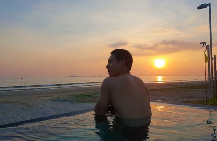Gay man at Rayong Marriott Resort & Spa infinity pool, enjoying a sunset. Thailand gay travel advice. Beach view. Relaxing vacation.