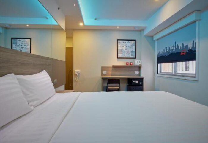 Red Planet Bangkok Surawong hotel room. Gay-friendly hotel with bed, desk, and city skyline window shade. Modern, clean design.