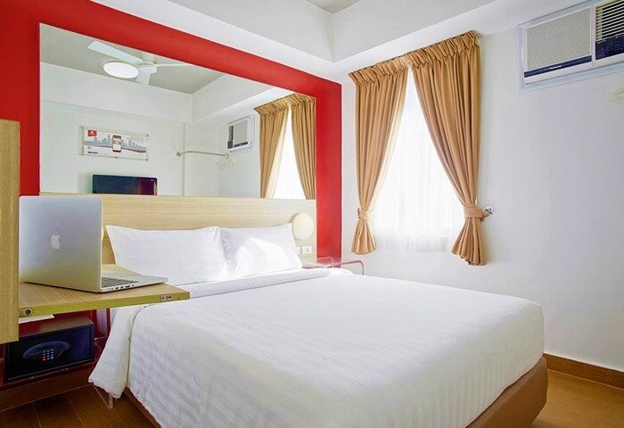 Red Planet Quezon Timog gay-friendly hotel room. Interior view with bed, laptop, and window. Modern design for LGBTQ+ travelers in Quezon City.