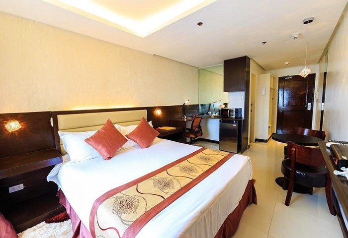 Regency Grand Suites gay-friendly hotel room. Queen bed with red pillows, desk, mini fridge, and dining table. Modern suite for gay travelers.
