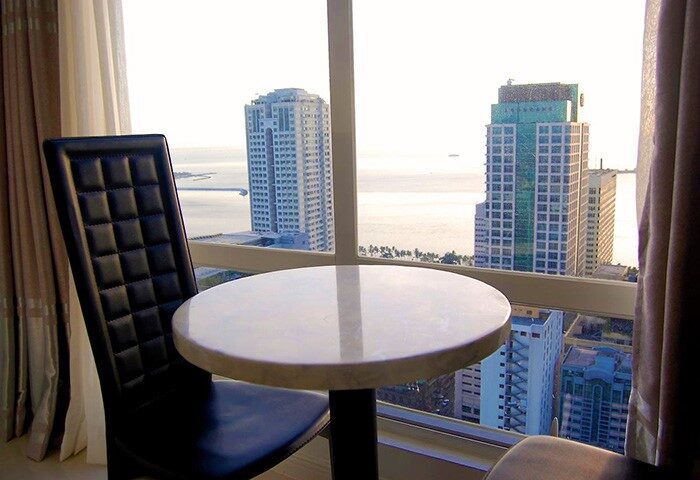 Regency Grand Suites gay-friendly hotel room view. Table and chair by window overlooking city skyline and ocean. Modern, upscale accommodations.