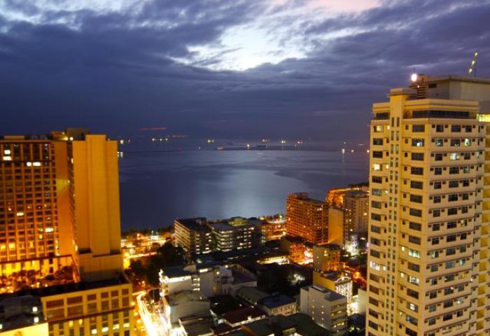 Night view from Regency Grand Suites, a gay-friendly hotel. City lights meet the sea under a cloudy sky. Manila travel for gay men.