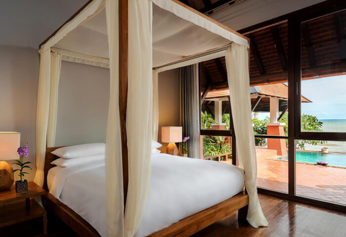 Bedroom view at Renaissance Koh Samui Resort & Spa, a gay-friendly hotel. Four-poster bed, pool, and ocean view.