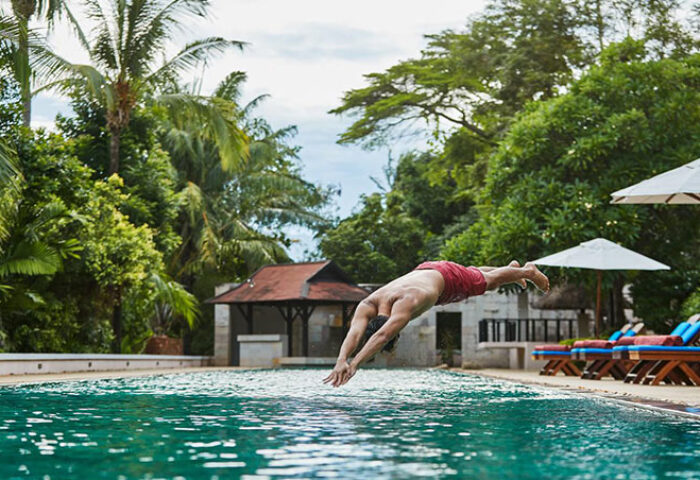 Man dives into pool at Renaissance Koh Samui Resort & Spa. Gay-friendly hotel with lush tropical surroundings. Relaxing gay travel destination.