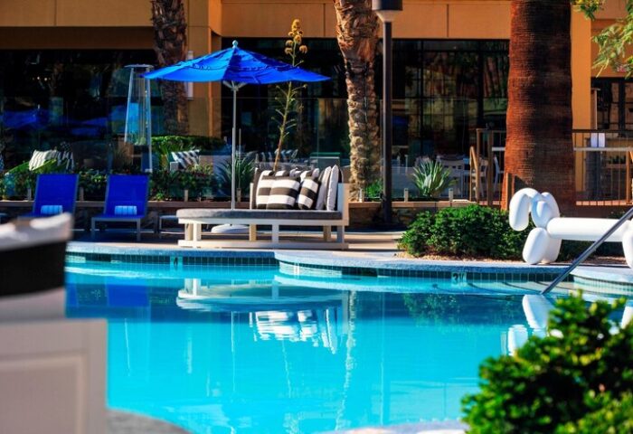 Poolside at Renaissance Palm Springs Hotel, a gay-friendly hotel. Blue umbrella, lounge chairs, and a whimsical balloon dog statue add to the resort's charm.