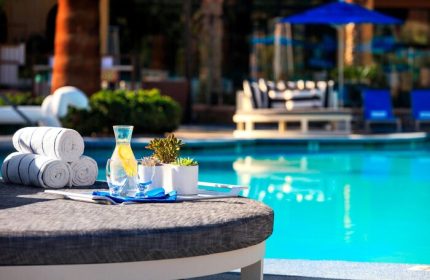 Poolside view at the gay-friendly Renaissance Palm Springs Hotel. Towels, water, and plants sit on a table near the pool.