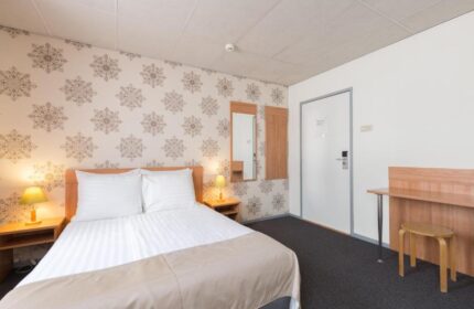 Rho Hotel's gay-friendly room. Double bed with bedside tables and lamps. Desk with stool. Wallpaper with snowflake pattern. Comfortable stay.