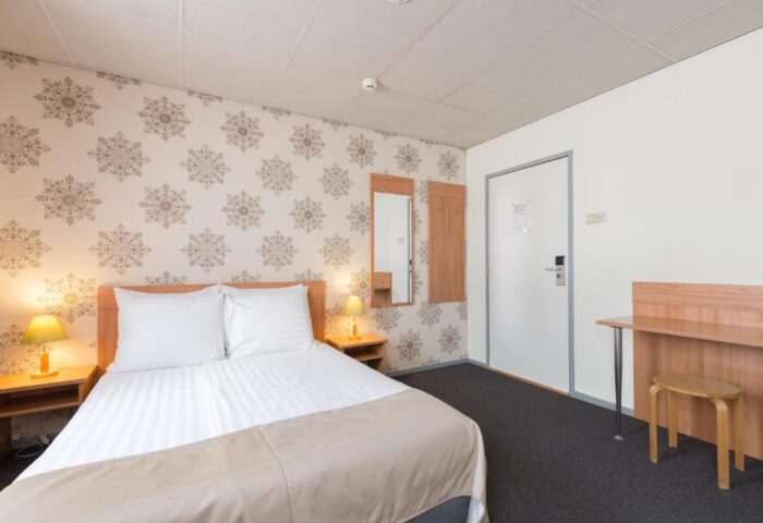 Rho Hotel's gay-friendly room. Double bed with bedside tables and lamps. Desk with stool. Wallpaper with snowflake pattern. Comfortable stay.