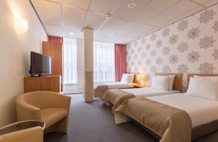 Gay-Friendly Rho Hotel room with three beds, armchair, TV, and snowflake wallpaper. A comfortable stay for gay men travelers.