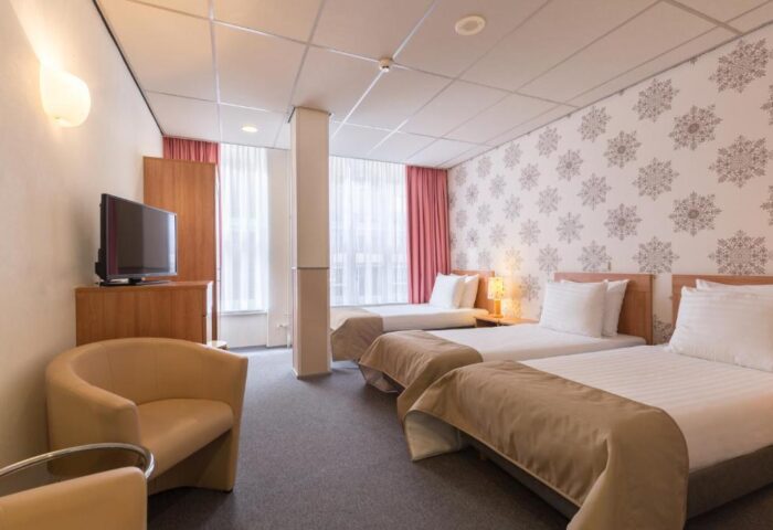 Gay-Friendly Rho Hotel room with three beds, armchair, TV, and snowflake wallpaper. A comfortable stay for gay men travelers.