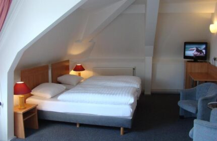 Rho Hotel gay-friendly room. Twin beds under a sloped ceiling. Nightstands with lamps, TV, and armchairs. Comfortable stay for gay travelers.