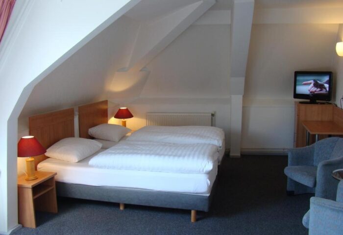 Rho Hotel gay-friendly room. Twin beds under a sloped ceiling. Nightstands with lamps, TV, and armchairs. Comfortable stay for gay travelers.
