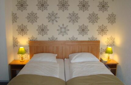 Gay-Friendly Rho Hotel room with twin beds, wooden headboard, patterned wallpaper, bedside tables, and lamps. Comfortable stay for gay travelers.